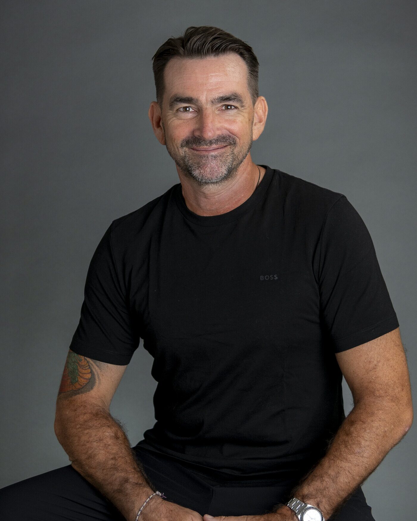 Morgan Meinecke, seated, in a black t-shirt against a grey studio backdrop